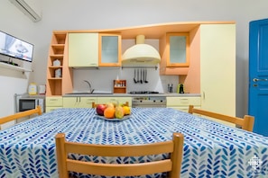 A compact kitchen with a microwave, stove, and sink, a dining table with a fruit bowl, and a blue door.