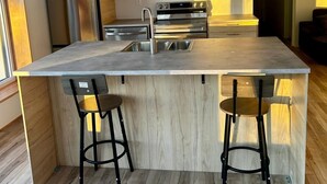 A modern kitchen with a central island, stainless steel appliances, wooden cabinets, and a bar stool seating area.