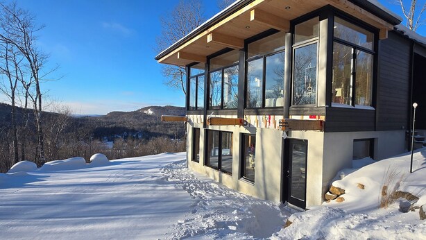 A modern building with large windows, a wooden deck, and a snowy landscape in the background.