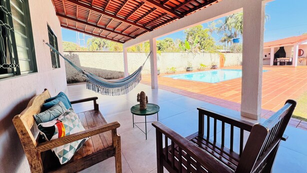 Une terrasse couverte avec un hamac, des meubles en bois et une vue sur une piscine.