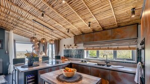 A modern kitchen with a bamboo ceiling, a central island with a bowl of fruit, and a view of the outdoors through large windows. - 2 Bed in Pensilva (oc-s30446) (Pensilva)