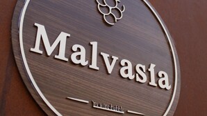 Segno circolare con il nome "Malvasa" e il logo di una vite, fissato su una parete marrone.