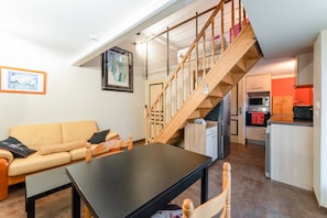 Un salon comprenant un canapé, une table à manger, un escalier en bois et un coin cuisine équipé d’appareils électroménagers modernes.