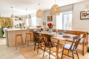 A modern kitchen with a central island, bar stools, wooden chairs, and pendant lighting. - 3 Bed in Horton (oc-s30500) (Port Eynon)