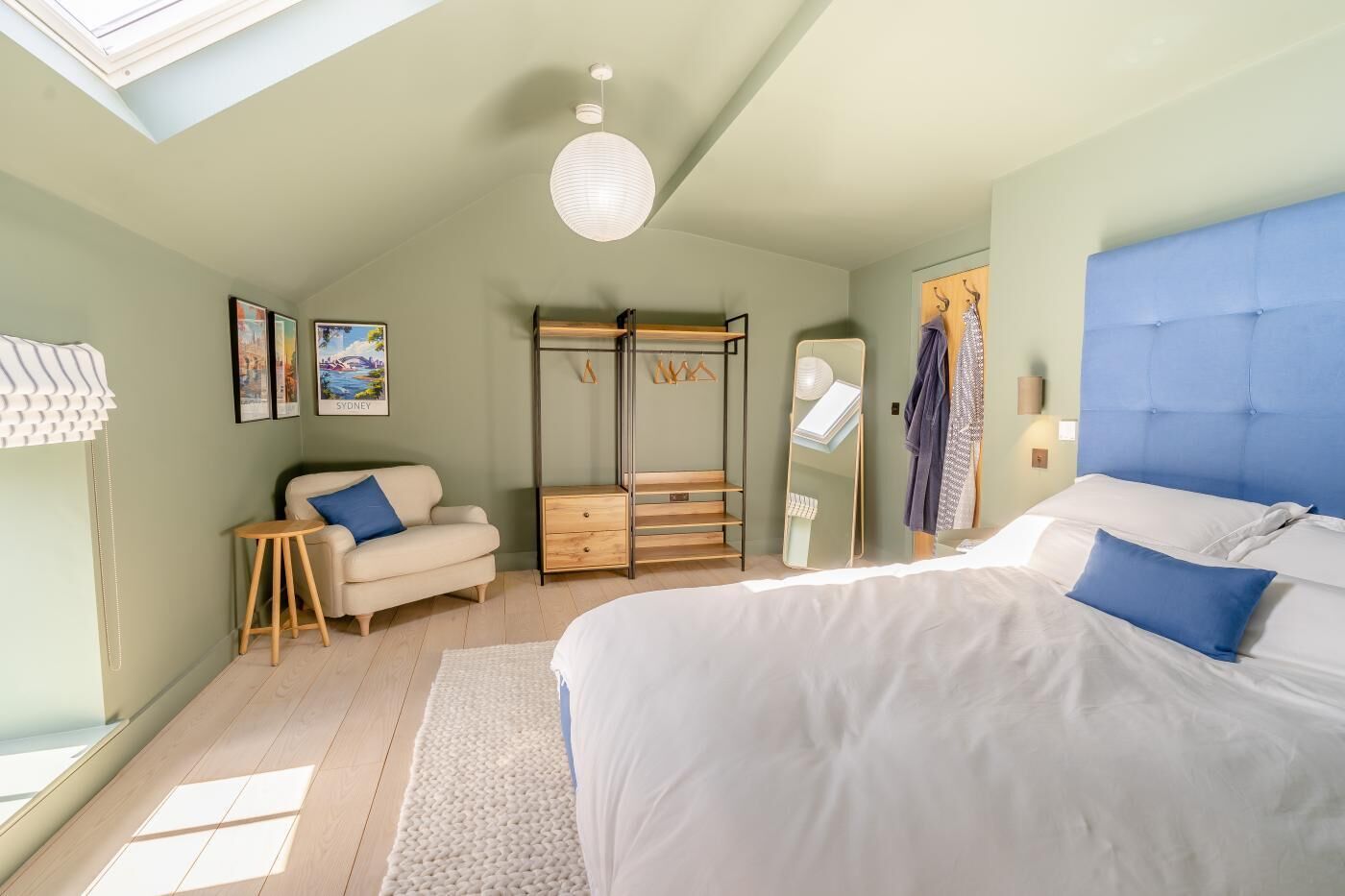 A bedroom with a bed, a sofa, a wardrobe, a mirror, and a hanging light fixture.