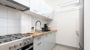 Kompakti keittiö, jossa on valkoiset kaapit, ruostumattomasta teräksestä valmistettu liesi ja puinen työtaso.