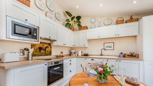 A modern kitchen with white cabinetry, a microwave, a toaster, and a dining area with a wooden table set for two. - 1 Bed in Ashton (oc-p30484) (Ashton)