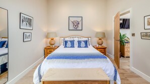 A bedroom with a large bed, two bedside tables, a bench, and a door leading to another room. - 1 Bed in Ashton (oc-p30484) (Ashton)