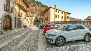 Una strada acciottolata fiancheggiata da edifici tradizionali, auto parcheggiate e un cielo sereno.