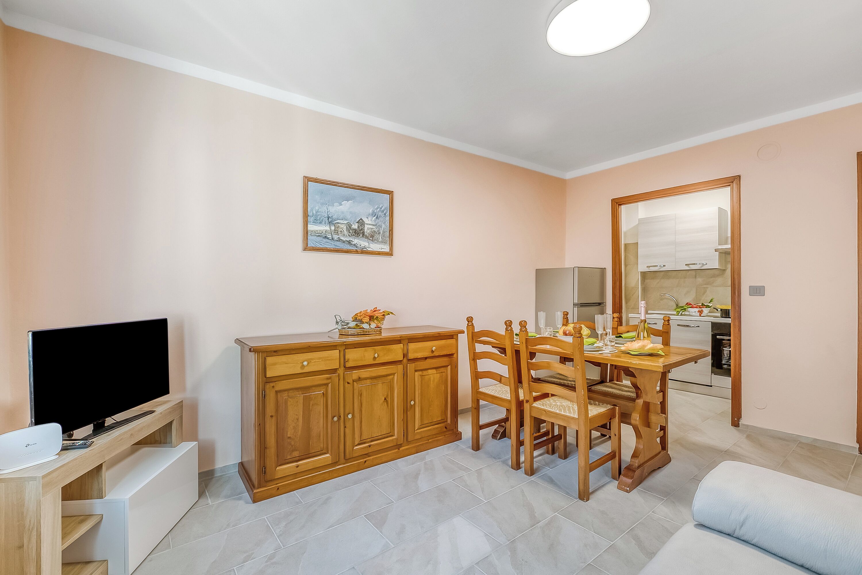 A compact living space with a TV, wooden cabinet, dining table, and chairs.