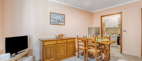A compact living space with a TV, wooden cabinet, dining table, and chairs.