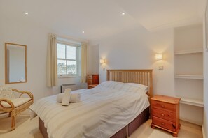 A bedroom with a bed, a wooden nightstand, a chair, a mirror, and a window with curtains. - 2 Bed in Polruan (oc-g30534) (Fowey)