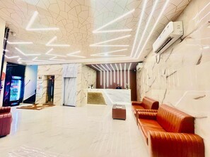 A modern lobby with a marble reception desk, a red leather sofa, and a vending machine. - Hotel Sm Eagle Grand Airport Zone Hyd (Hyderabad)