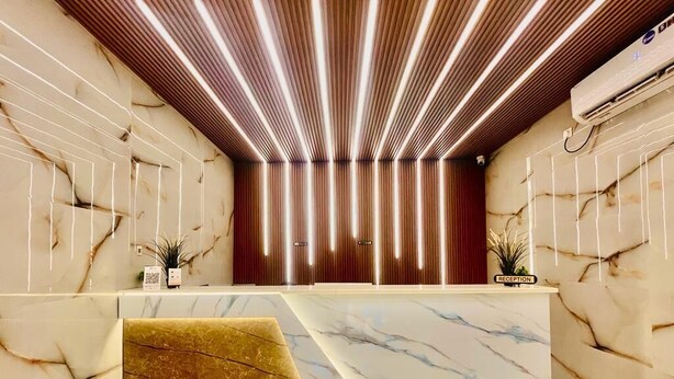 A reception area with a marble counter, vertical wooden slats on the ceiling, and a reception desk labeled "RECEPTION". - Hotel Sm Eagle Grand Airport Zone Hyd (Hyderabad)