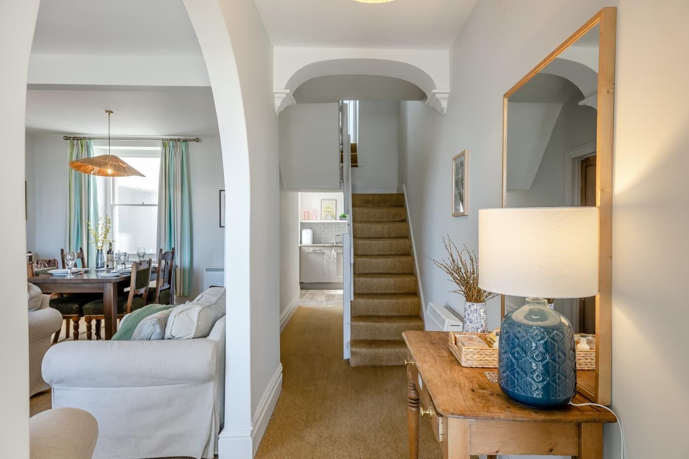 A living room with a sofa, a dining area with a table and chairs, a staircase, and a mirror.