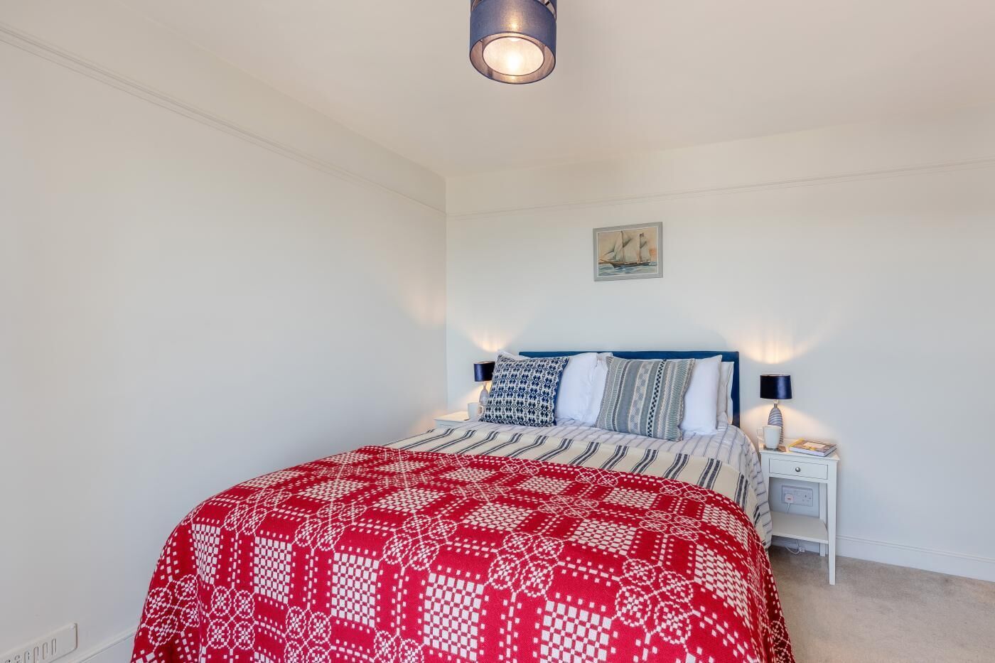 Ein Schlafzimmer mit einem Bett, Nachttischlampen, einem Nachttisch, einem Wandbild und einer Deckenleuchte.