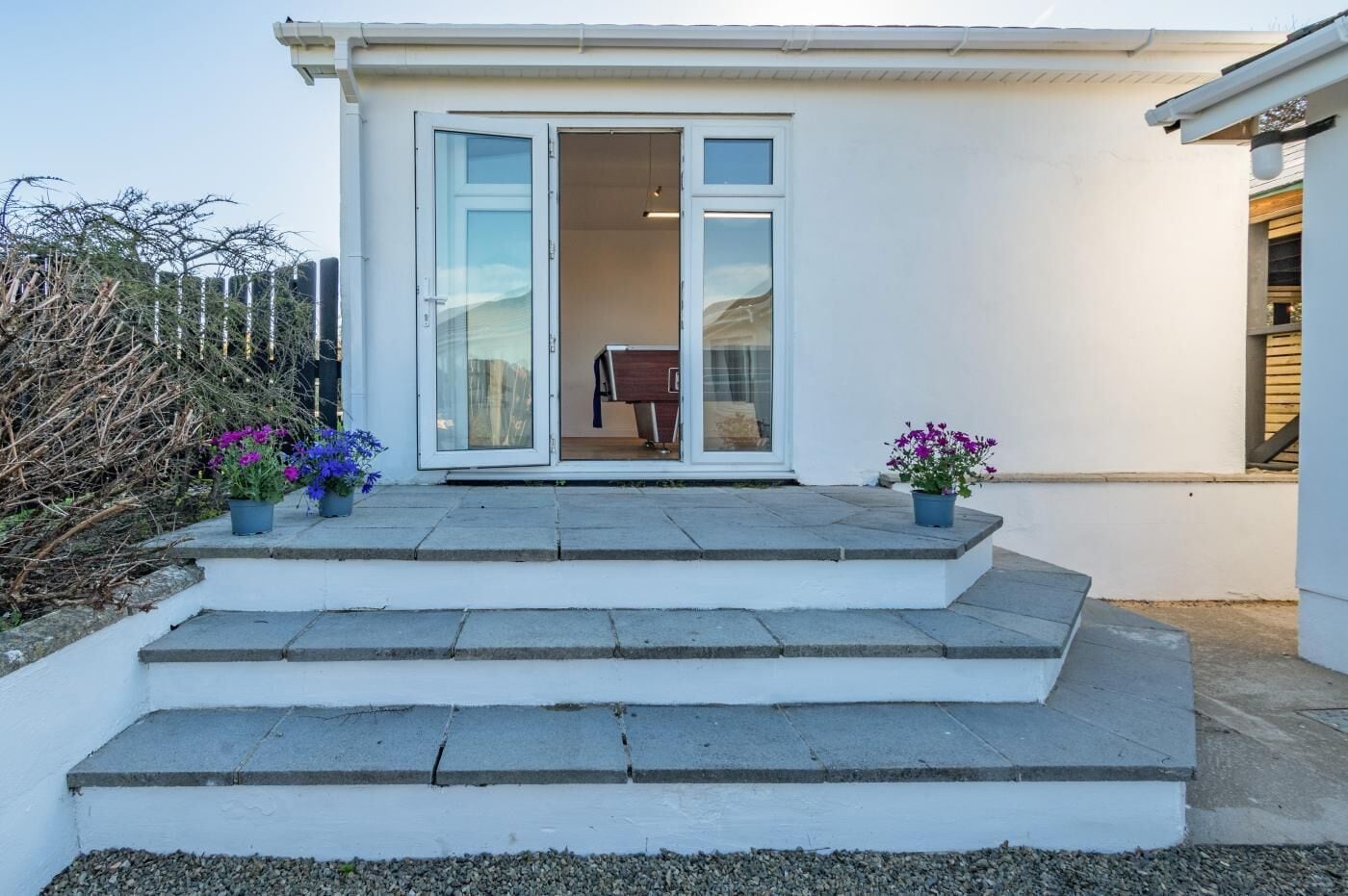 Una casa moderna con fachada blanca, puerta de cristal y un pequeño porche con escalones que conducen a la entrada.