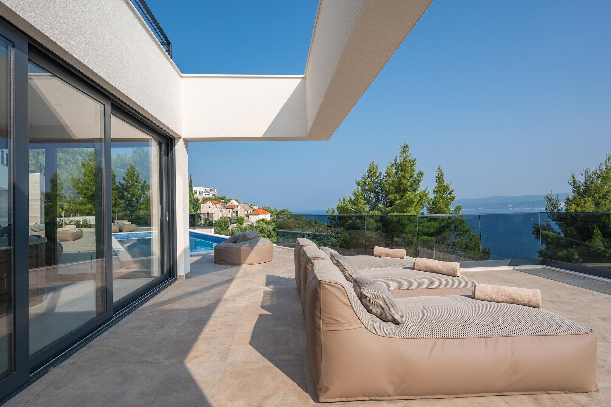A modern outdoor living area with a pool, lounge chairs, and a view of the sea.