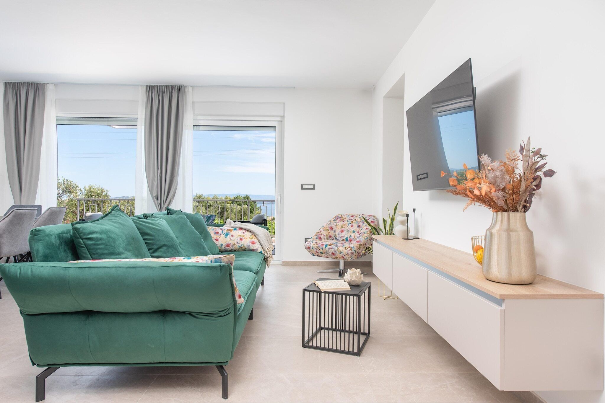 A modern living room with a green sofa, a small side table, a decorative vase, and a flat-screen TV mounted on the wall.