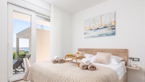 A bedroom with a bed, a painting, a bedside table, and a view of the outside. - Charming Seaside Villa Getaway (Splitsko-dalmatinska župani)