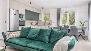 A modern kitchen with a refrigerator, oven, and microwave. There is a dining area with a table and chairs. A green sofa with a floral pillow is in the foreground. - Charming Seaside Villa Getaway (Splitsko-dalmatinska župani)
