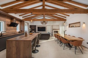 A modern kitchen with a wooden ceiling, a central island, and a dining area with a long table and chairs.