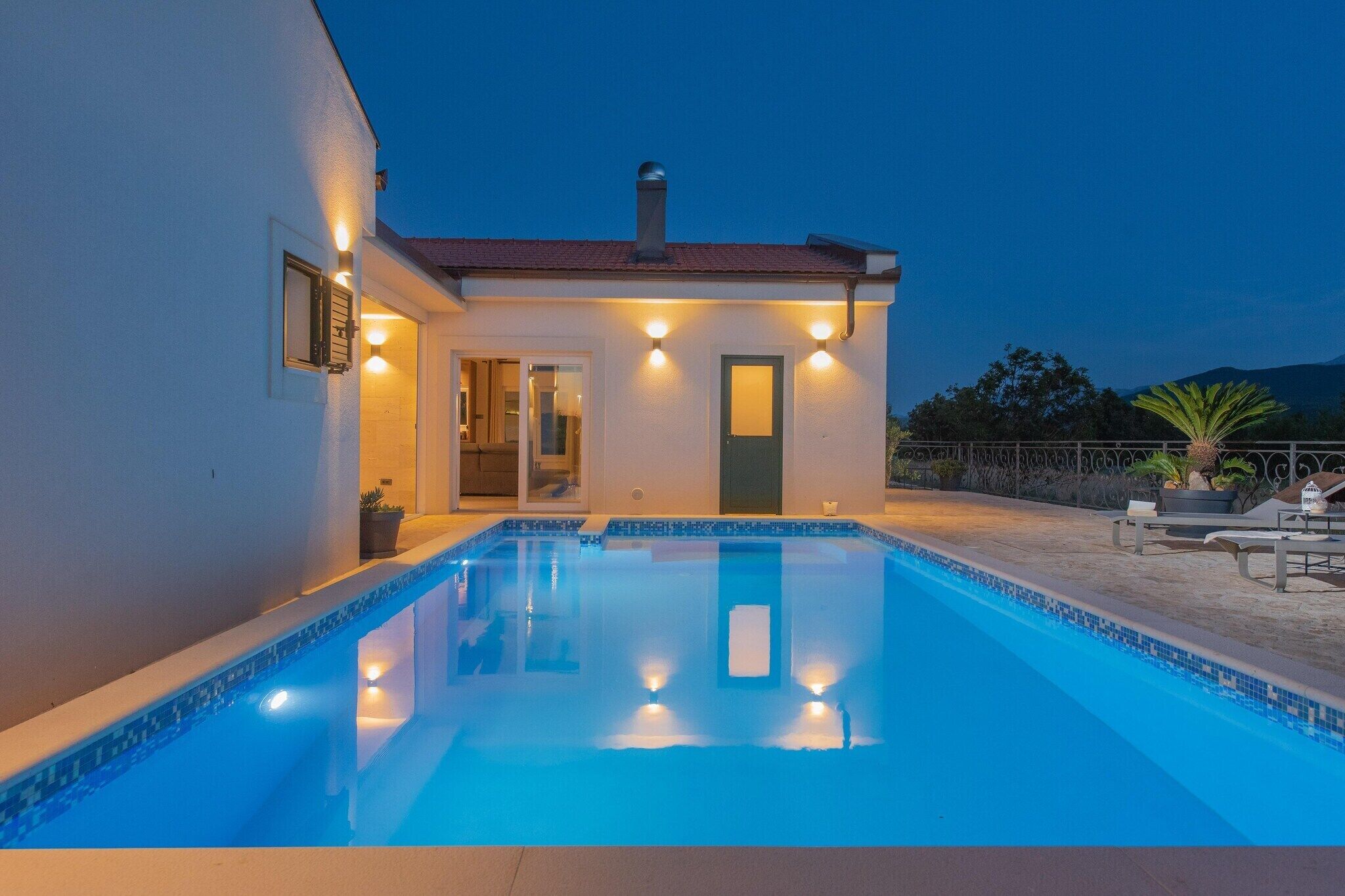 A swimming pool with a clear blue edge, a small building with a door and windows, and a patio area with outdoor furniture.