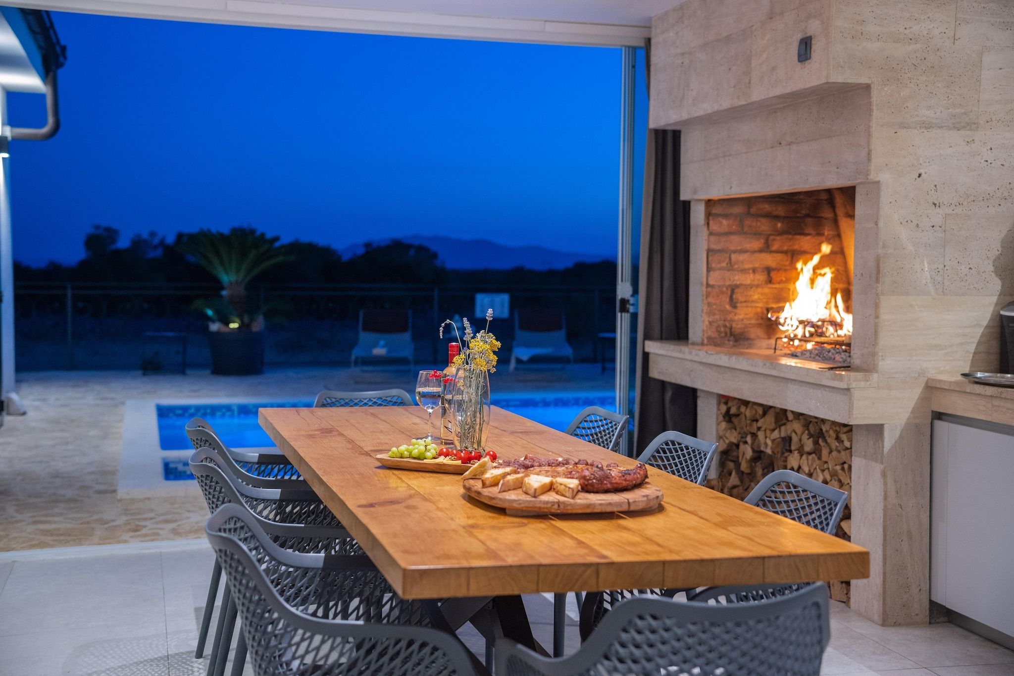 An outdoor dining area with a wooden table, chairs, and a fire feature.