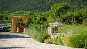Un chemin pavé mène à une pergola en bois, adossée à un mur de pierres et agrémentée de verdure.