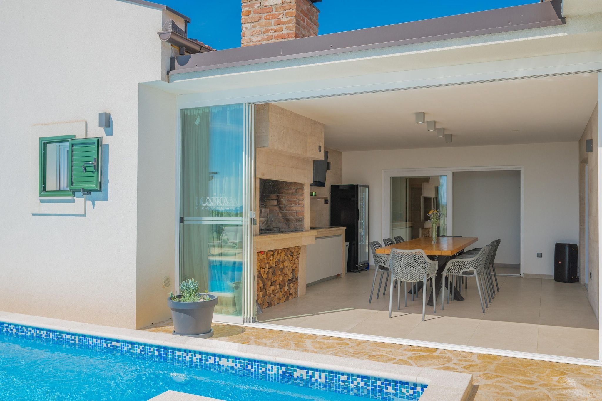 Un espacio exterior moderno con piscina, mesa de comedor y cocina.