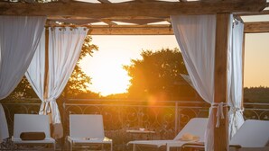Un espace aménagé au bord de la piscine, avec des chaises longues blanches, une table et une vue sur le coucher de soleil.