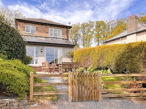 Ein zweistöckiges Haus mit einer Terrasse, Holzmöbeln und einer Steinmauer.