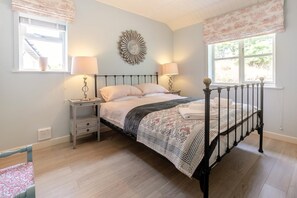Un dormitori amb un llit amb cortines, taules de nit amb làmpades, un element decoratiu a la paret i una finestra amb cortines.