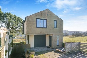 Ein zweigeschossiges Steinhaus mit Garage, einer kleinen Veranda und einem umzäunten Garten.