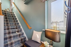 Eine Treppe mit einem Karokarpete, einem weißen Kissen, einer Lampe und einem Fenster mit Jalousien.