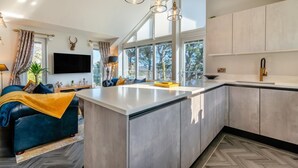 A modern kitchen with a central island, large windows, and a cozy seating area with a blue sofa. - 2 Bed in Barrowford (oc-w30592) (Barrowford)