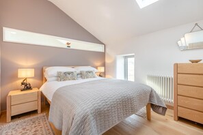 Une chambre à coucher comprenant un lit, des tables de chevet, une commode, un radiateur et un puits de lumière.