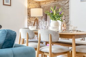 Un coin repas avec un mur en pierre, une table dressée avec des assiettes, des verres et une bouteille de vin.