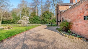 A gravel driveway leading to a brick building with chimneys, surrounded by trees and a picnic table. - 2 Bed in Southwell (oc-n30605) (Southwell)
