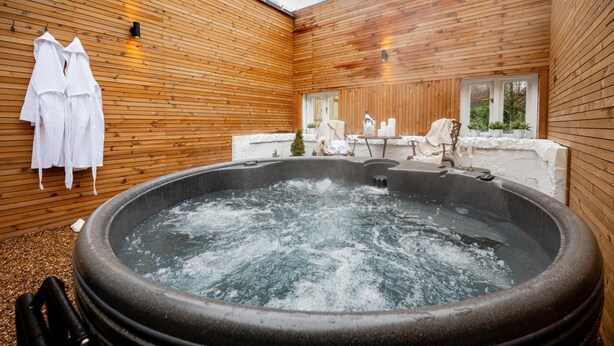 A hot tub in a wooden room with a window, a chair, and a table. - 2 Bed in Southwell (oc-n30605) (Southwell)