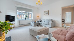 A modern living room with a large window, a flat-screen TV, a sofa, a coffee table, and a pink chair. - 2 Bed in Eastbourne (oc-b30385) (Eastbourne)
