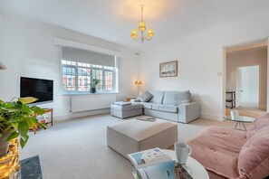A modern living room with a large window, a flat-screen TV, a sofa, a coffee table, and a pink chair. - 2 Bed in Eastbourne (oc-b30385) (Eastbourne)