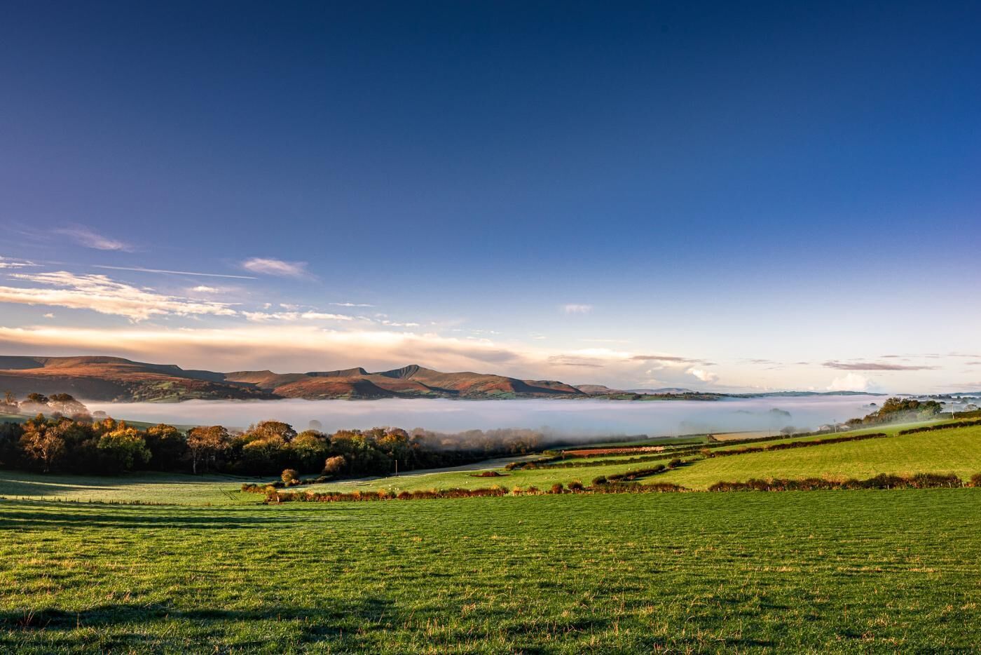 A panoramic view of a rural landscape with rolling hills, a mist-covered lake, and a clear sky.