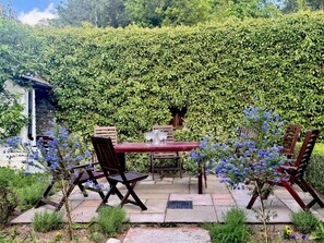 Ein Sitzbereich im Freien mit Tisch und Stühlen, umgeben von einer üppigen, grünen Hecke.
