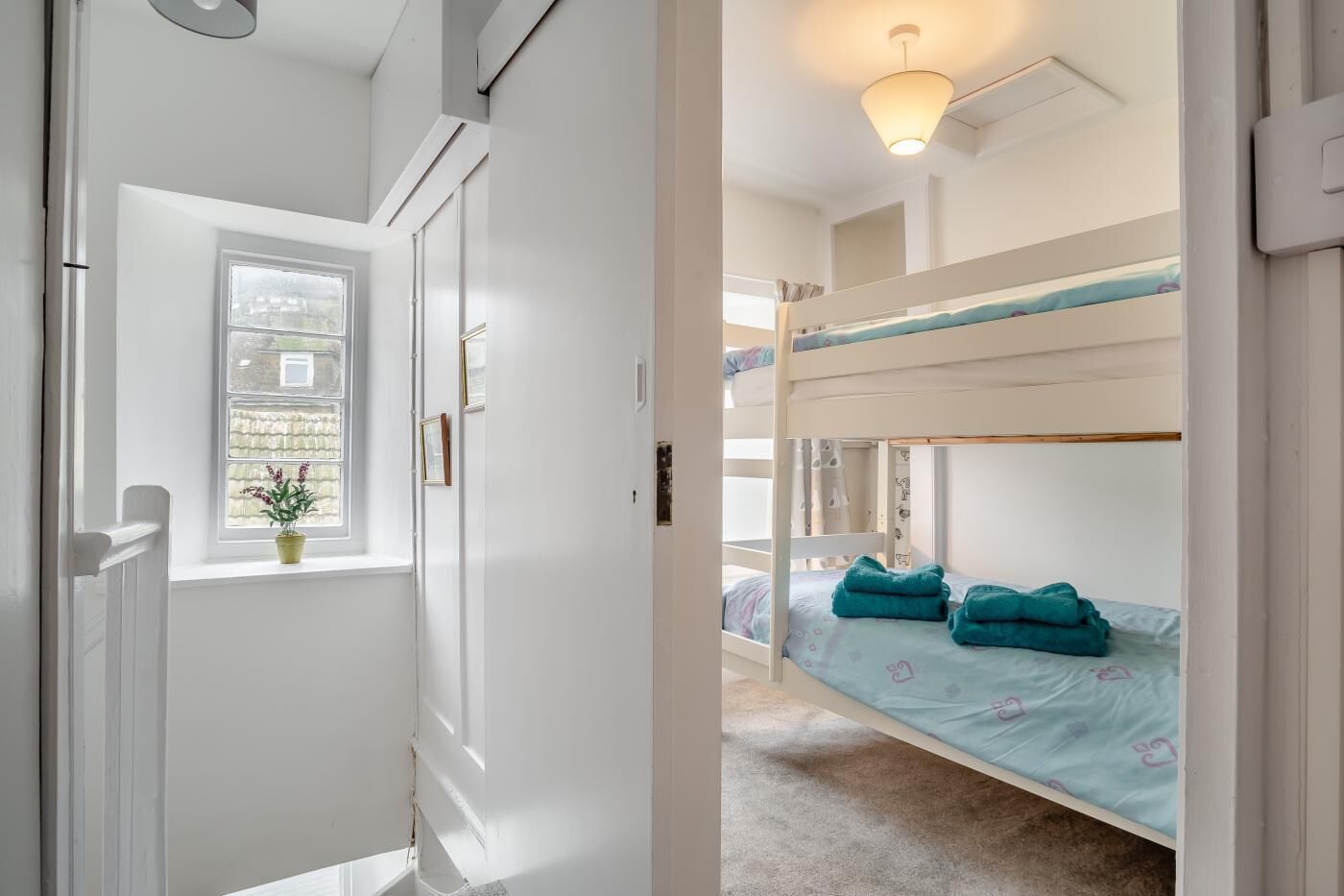 Ein Zimmer mit Etagenbetten, einem Fenster mit Pflanze und einer Deckenleuchte.