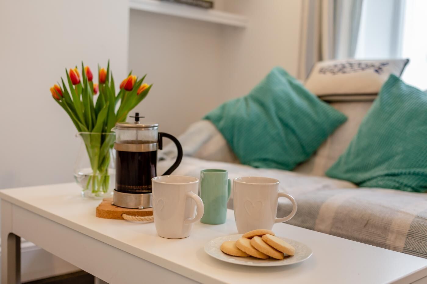 A cozy living area with a coffee maker, a plate of cookies, and a vase of tulips on a white table.