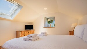 Une chambre à coucher avec un grand lit, une commode en bois, un téléviseur et une fenêtre agrémentée d’une plante.