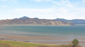 A coastal landscape with a beach, calm sea, and distant mountains. - 5 Bed in Bwlchtocyn (oc-s30770) (Bwlchtocyn)