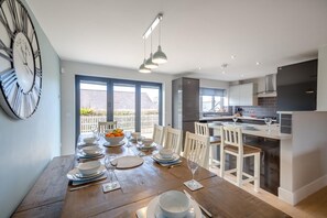 A modern kitchen with a dining area, featuring a large window, a clock, and a dining table set for four. - 5 Bed in Bwlchtocyn (oc-s30770) (Bwlchtocyn)