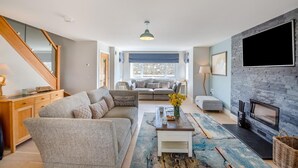 A modern living room with a sectional sofa, a coffee table, a fireplace, and a TV mounted on the wall. - 5 Bed in Bwlchtocyn (oc-s30770) (Bwlchtocyn)